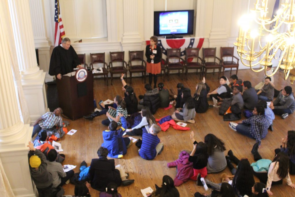 Justice Eveleigh talks to students from a podium.