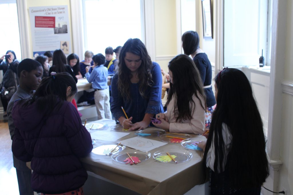 Students stand around a table writing down acts of kindness that they do.