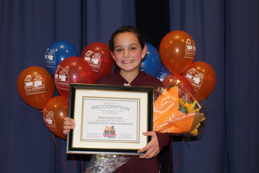 CTKG Megan stands with certificate of recognition in front of red, orange, and blue balloons.