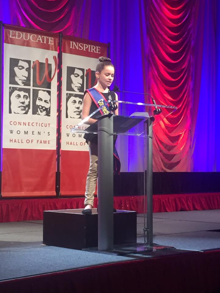CTKG Elena stands at a podium at the Connecticut Women's Hall of Fame to give a speech.